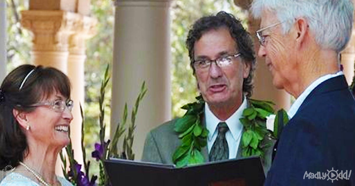 An outdoor wedding ceremony with three adults wearing formal attire, including a green leaf lei around one's neck. The setting includes natural daylight and greenery.