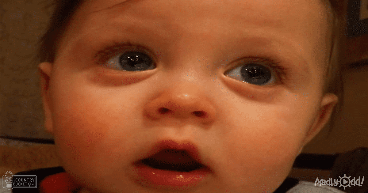 An infant male wearing a light-colored top with dark collar indoors under warm evening lighting.