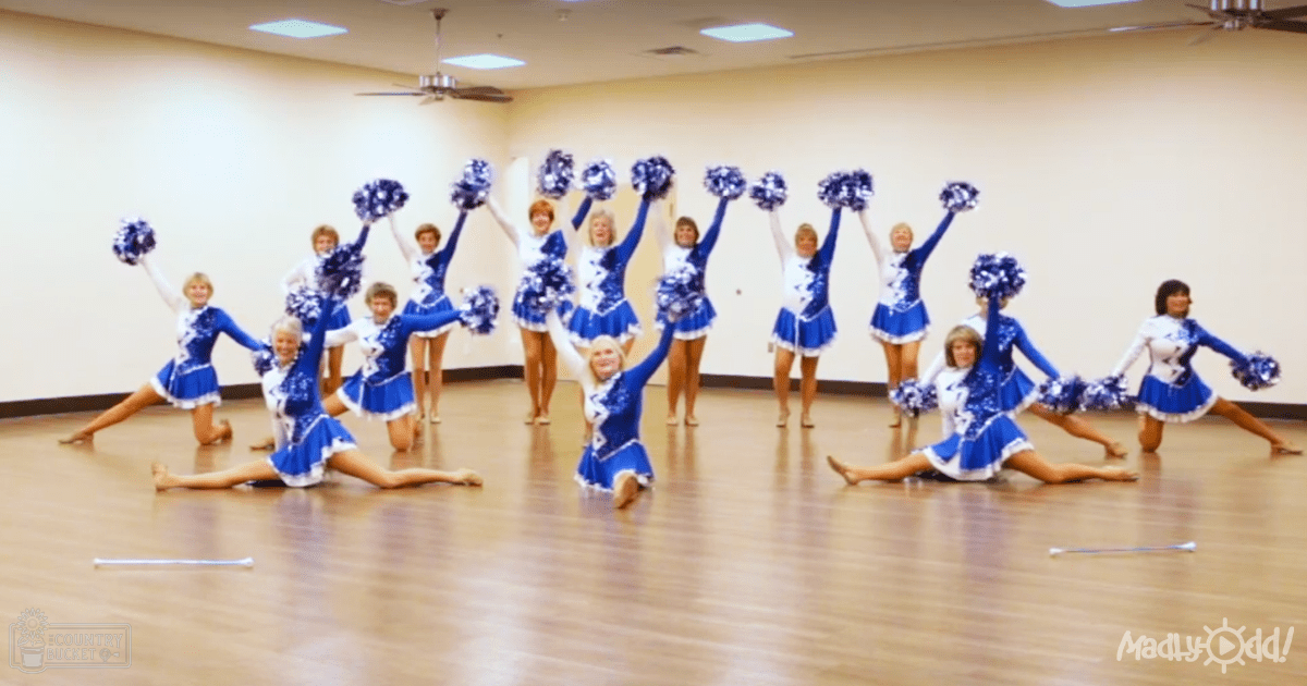 Group of young female cheerleaders in blue and white uniforms with pom-poms, cut-out skirts, long sleeves, high necklines, barefoot or wearing light-colored athletic shoes, performing in a dance studio.