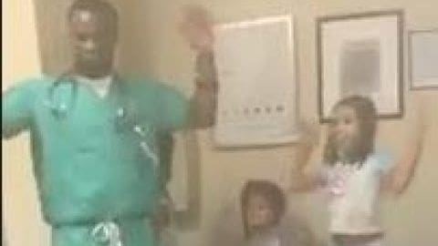 A medical professional wearing teal scrubs in a hospital setting, interacting with a young child.