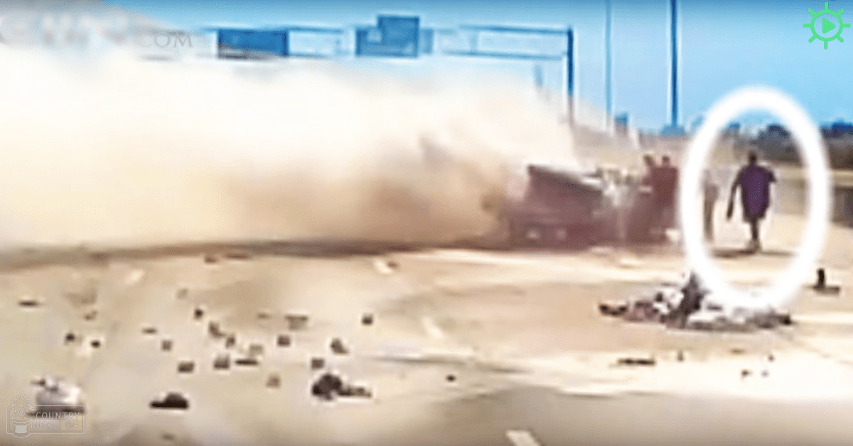 Explosion scene with a large cloud of smoke and debris, involving damaged heavy equipment; dusty industrial setting under clear skies.