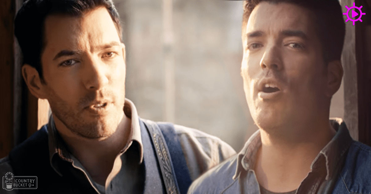 Two adult males in a rustic indoor setting with wooden beams and stone walls; one wears a light shirt under a denim vest.
