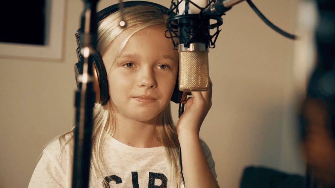 A young adult female wearing headphones and a 'CUP' T-shirt in a recording studio setting.