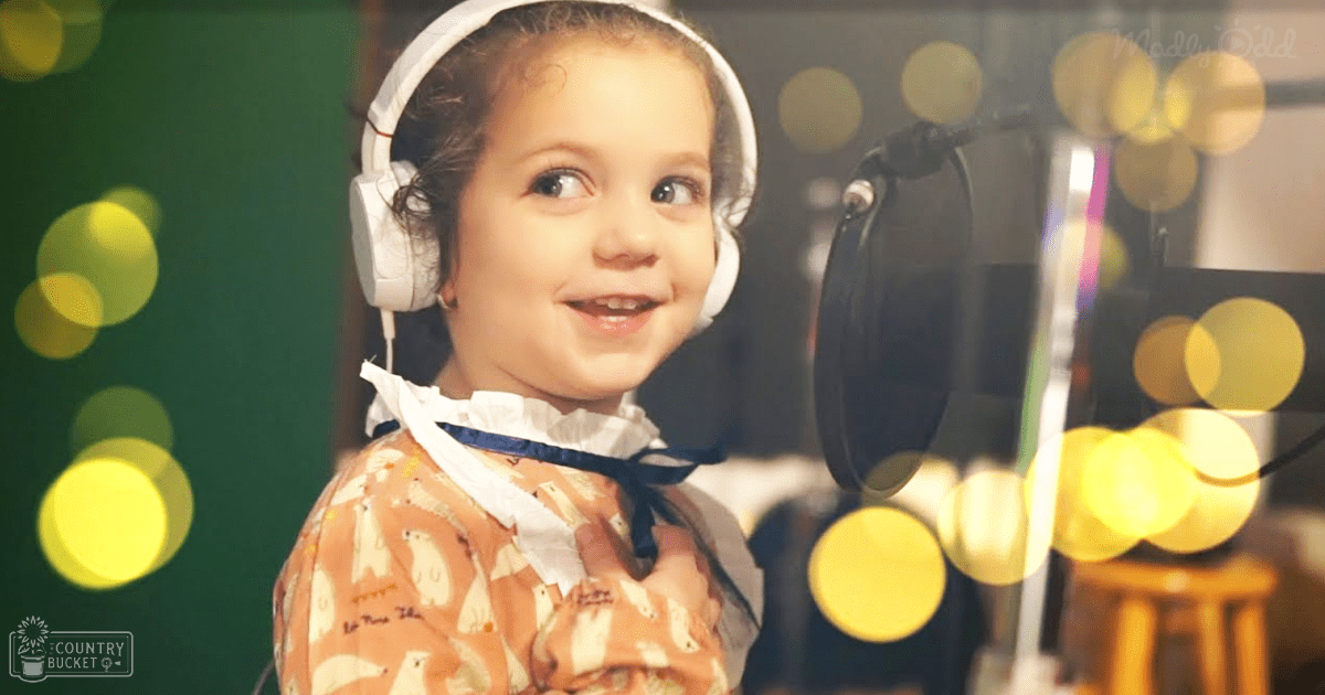 A toddler wearing white headphones, a ruffled collar shirt with blue ribbon, and an orange garment with polar bear pattern in a recording studio setting.