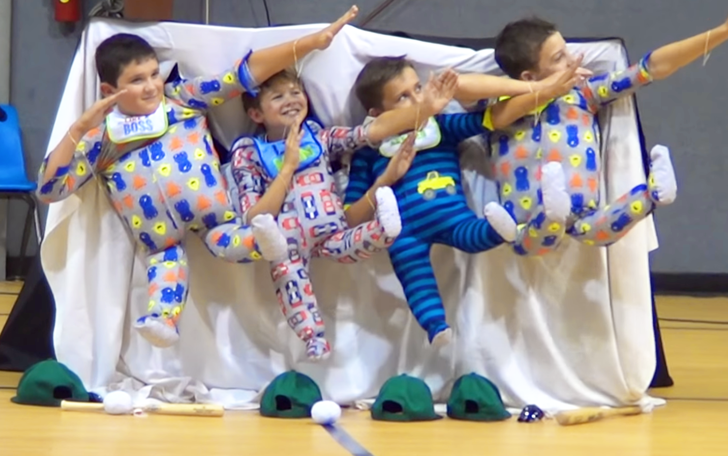 Children in pajamas performing in a gymnasium with sports equipment and neutral background.