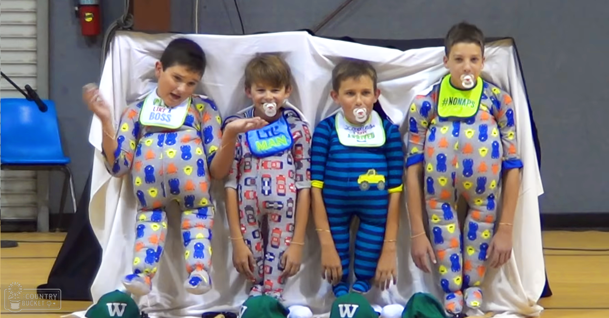 Children in pajamas standing indoors at an event with a backdrop and simple furniture.