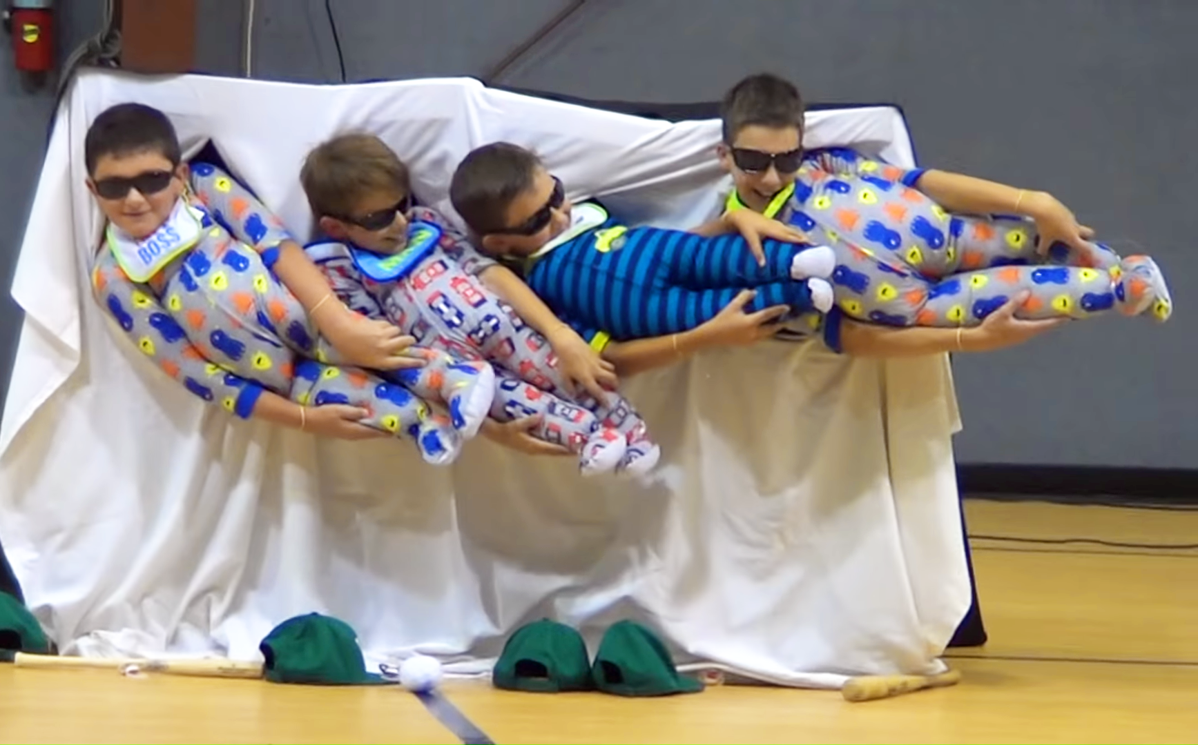 Young children in various colored pajamas being held by adults at an indoor gymnasium event.