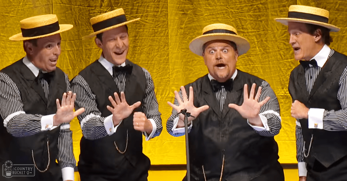 A group of adult male performers in stage attire holding microphones against a bright yellow backdrop, suggesting an indoor theatrical performance setting.