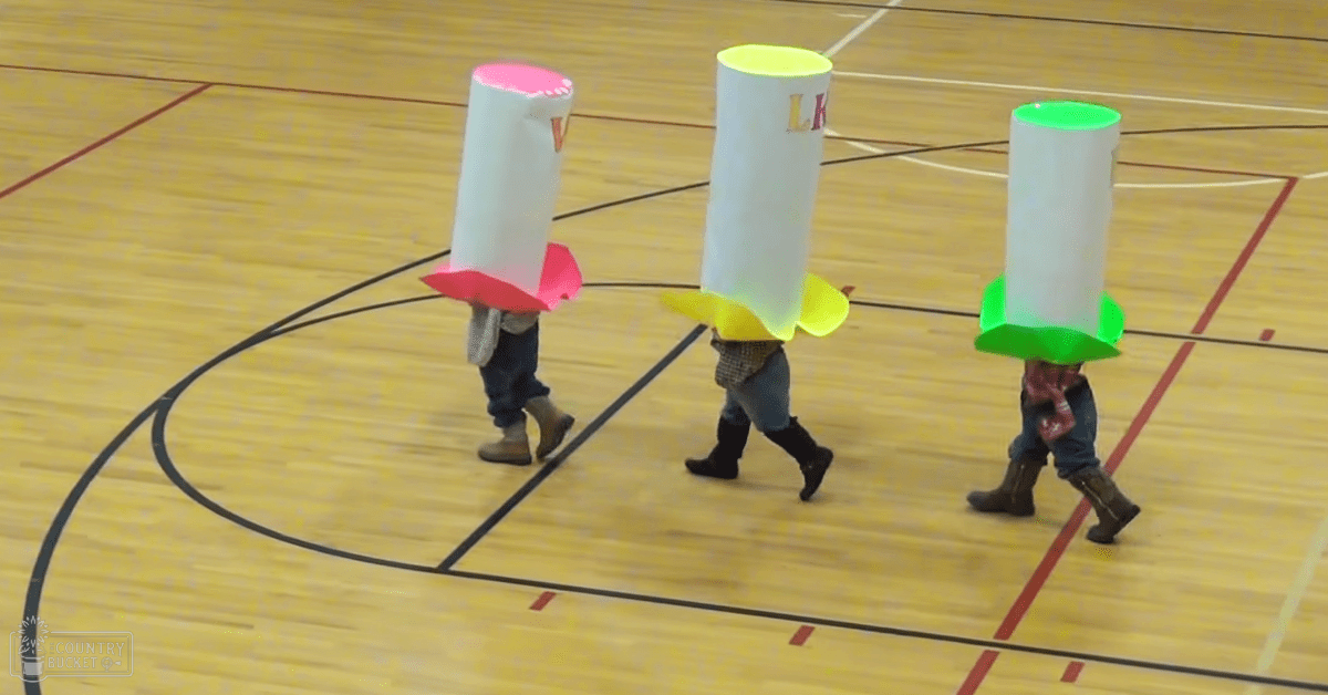 Children in rocket costumes at an indoor gymnasium with wooden floors marked for sports activities under soft lighting.