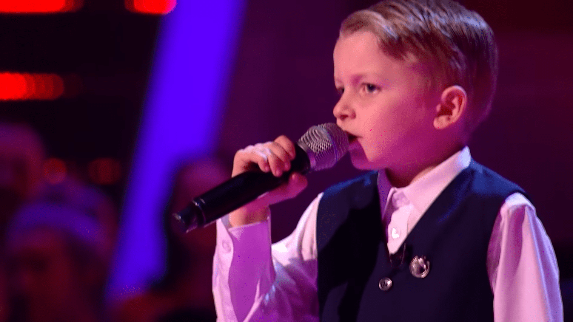 A young boy singing into a microphone in an indoor performance setting.