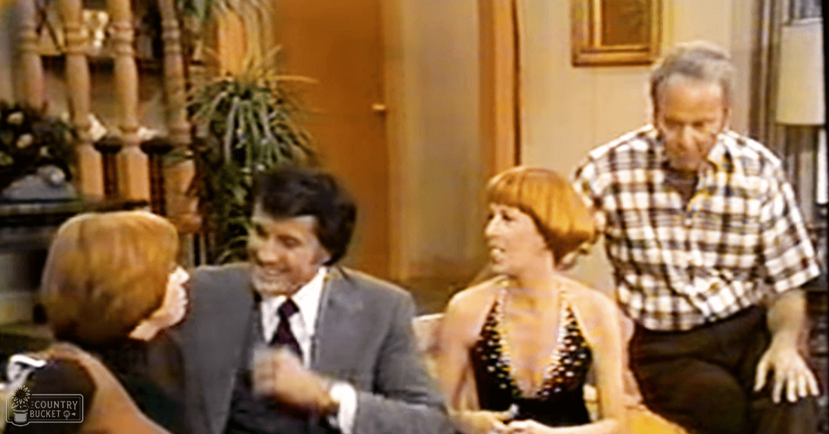 Adults engaged in conversation indoors, surrounded by furniture and plants, suggesting a relaxed home environment.