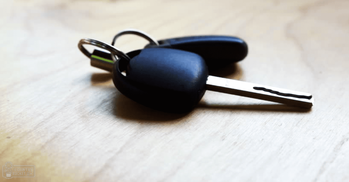 A set of car keys with black key fobs resting on a light wooden table, illuminated by natural daylight.