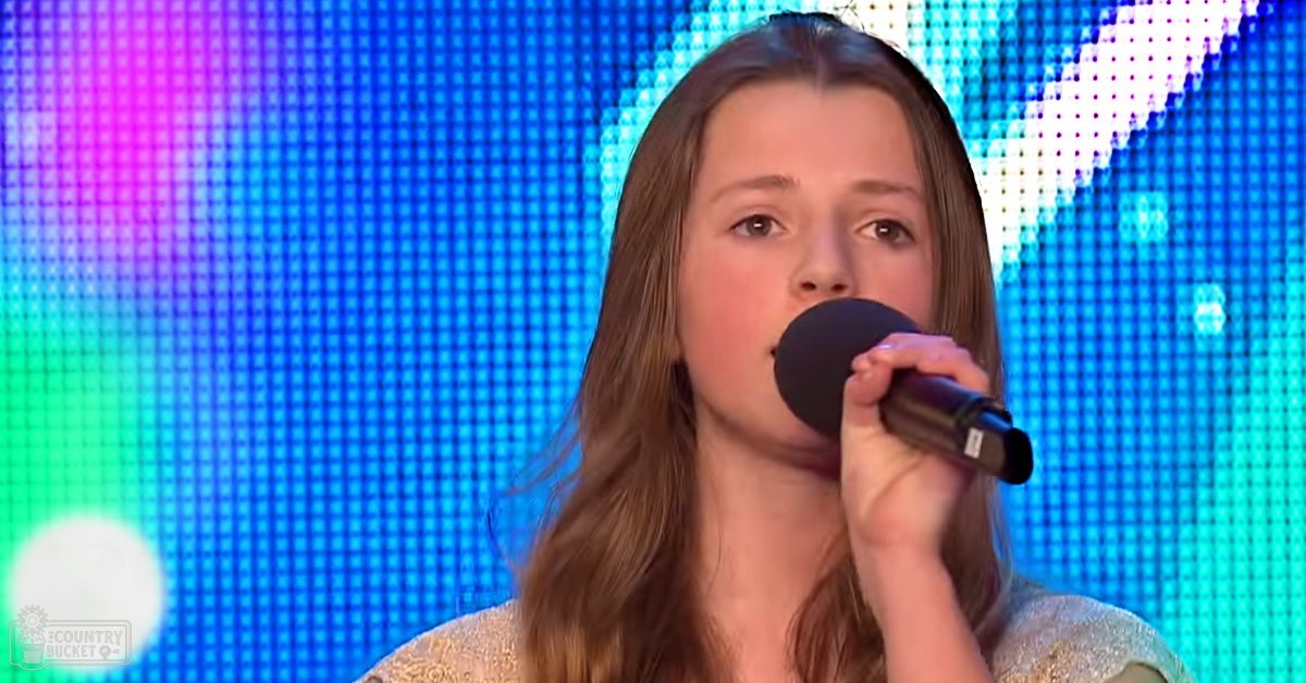 A young adult female singer performs on a brightly lit stage with vibrant LED screens displaying colors like blue, pink, and green.