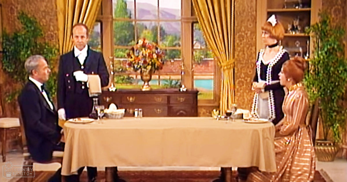 A historical drama scene set in an elegant dining room, with adults dressed in formal attire typical of the late 19th or early 20th century, with a focus on period furniture and decor.