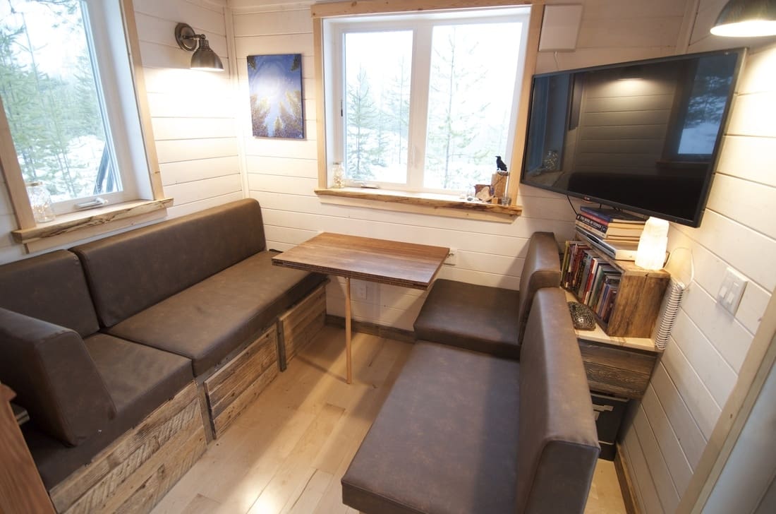 Snowy winter scene with cozy cabin interior, large windows, and relaxed living area.