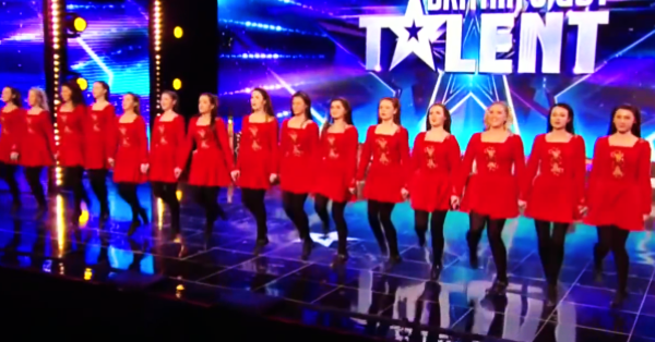Young adult female performers in red dresses with square necklines at a talent show stage with bright stage lighting and 'Talent' backdrop.