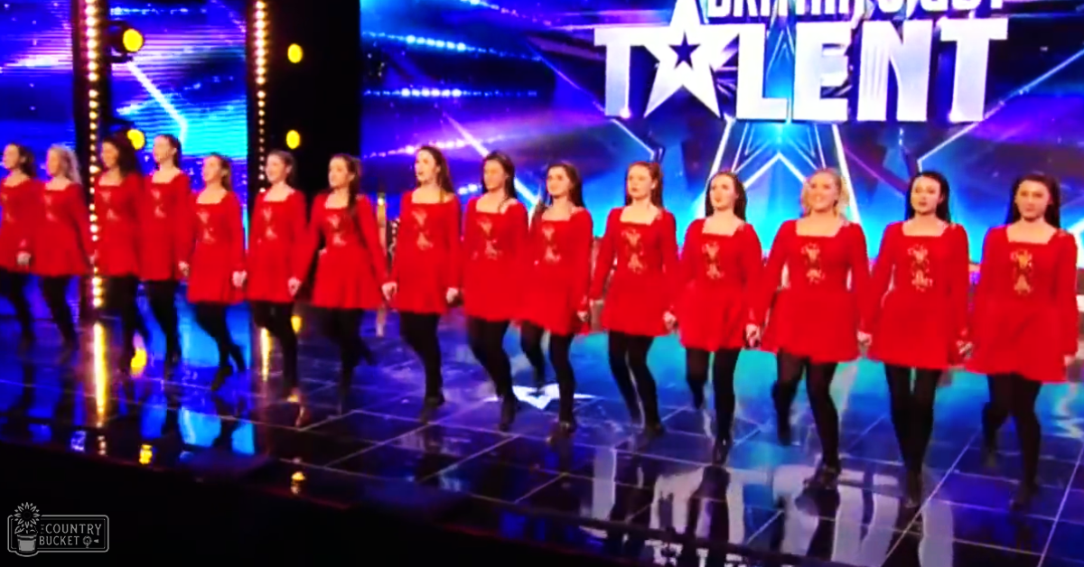 Young adult female performers in red dresses with square necklines, aA-line cut, and simple patterns on a Britain's Got Talent stage under bright studio lighting.