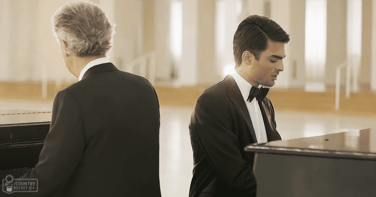Two men in formal attire stand on either side of grand pianos within a large room with high ceilings and large windows, suggesting it could be a concert hall or performance space; the setting is well-lit with soft diffused light indicating daytime or early evening.