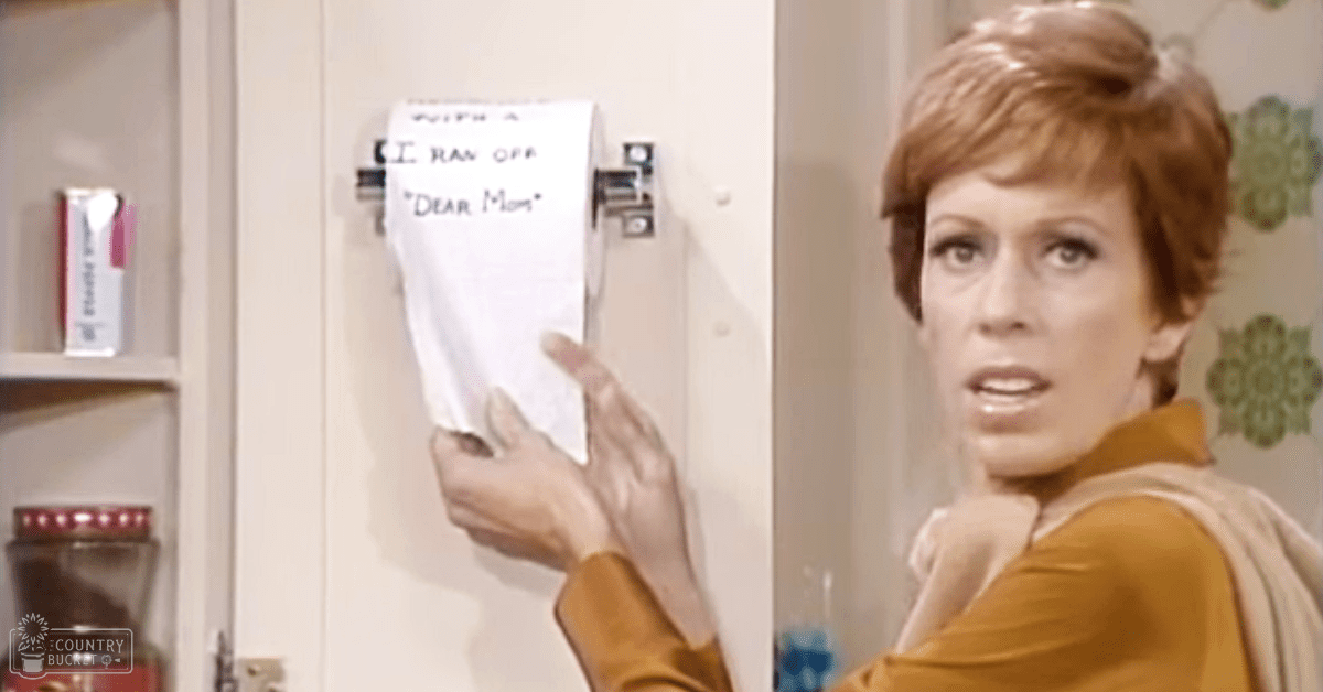 A mid-20th-century-style adult female wearing a mustard-yellow top with a wide collar and long sleeves, standing in what appears to be a kitchen setting. White cabinet doors with glass doors display items that might be kitchen supplies or medicine bottles.