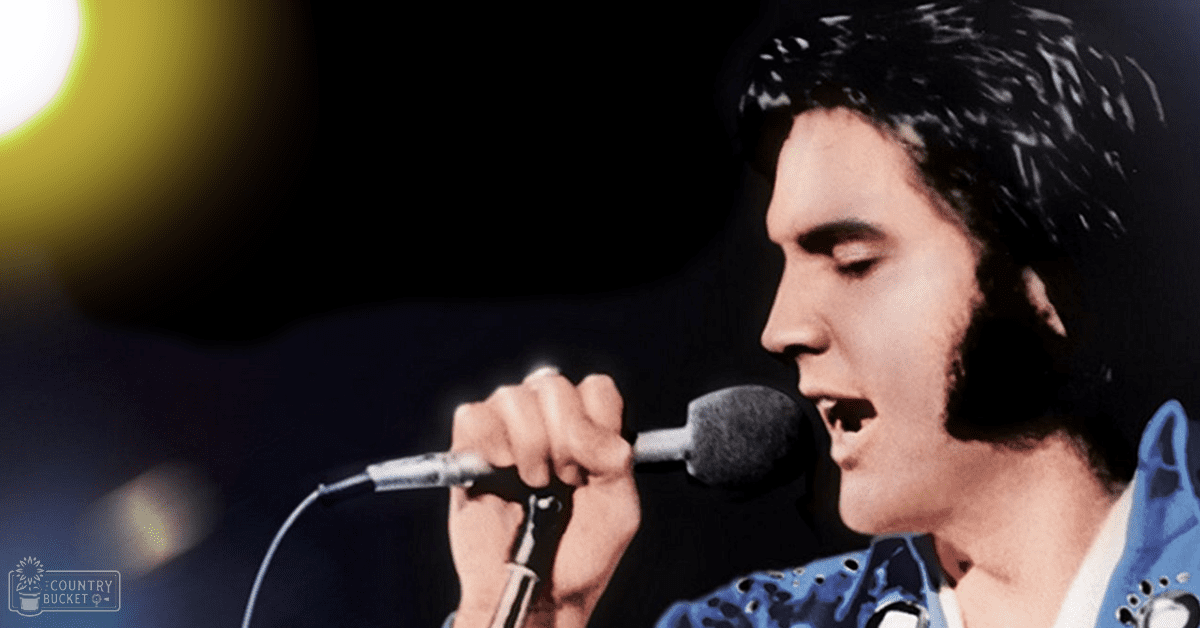 Adult male singer in a blue, white-dotted stage costume with high-cut neckline and puffed sleeves performs on an indoor stage under evening lighting.