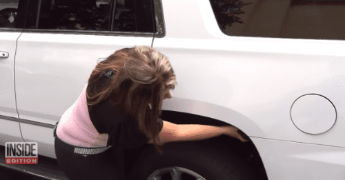 A young adult female wearing a black garment with short sleeves and a pink scarf stands outside near a white SUV. Inside Edition logo in the corner suggests news broadcast context.