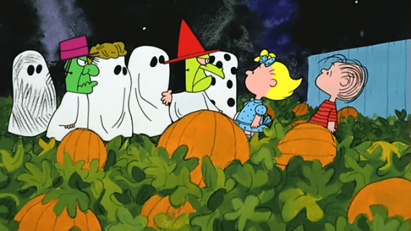 Children dressed in Halloween costumes amidst pumpkins under a starry night sky at a pumpkin patch during autumn.