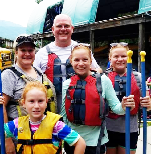 A family group at an outdoor recreational activity location with a school bus visible in the background.