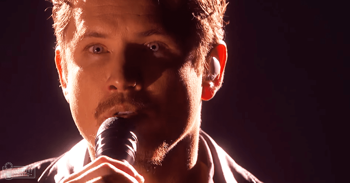 A young adult male performer on stage at a concert or similar event.
