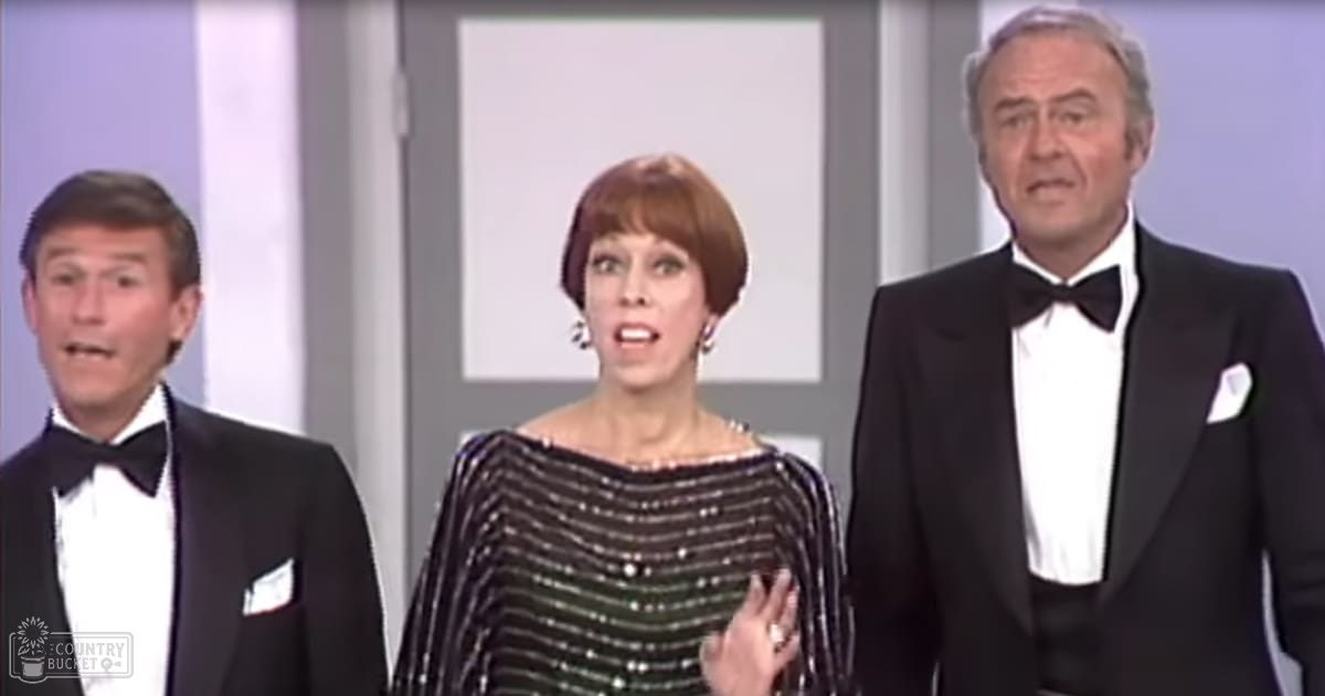 An indoor event setting with a woman in a black sequined dress at center, flanked by two men in tuxedos under artificial stage lighting.