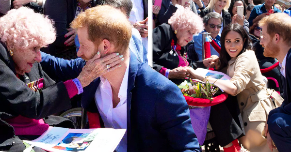Prince Harry and Meghan Markle interacting with an older adult female attendee during a public event, with the setting appearing to be Wellington.