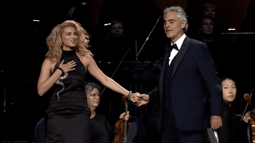 Two performers on stage at an evening concert; dark attire and formal setting highlight the musicians and orchestra.