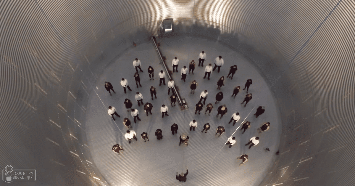 Young adults in a group activity inside an industrial silo, wearing white shirts and dark pants or skirts under natural daylight with corrugated metal walls.