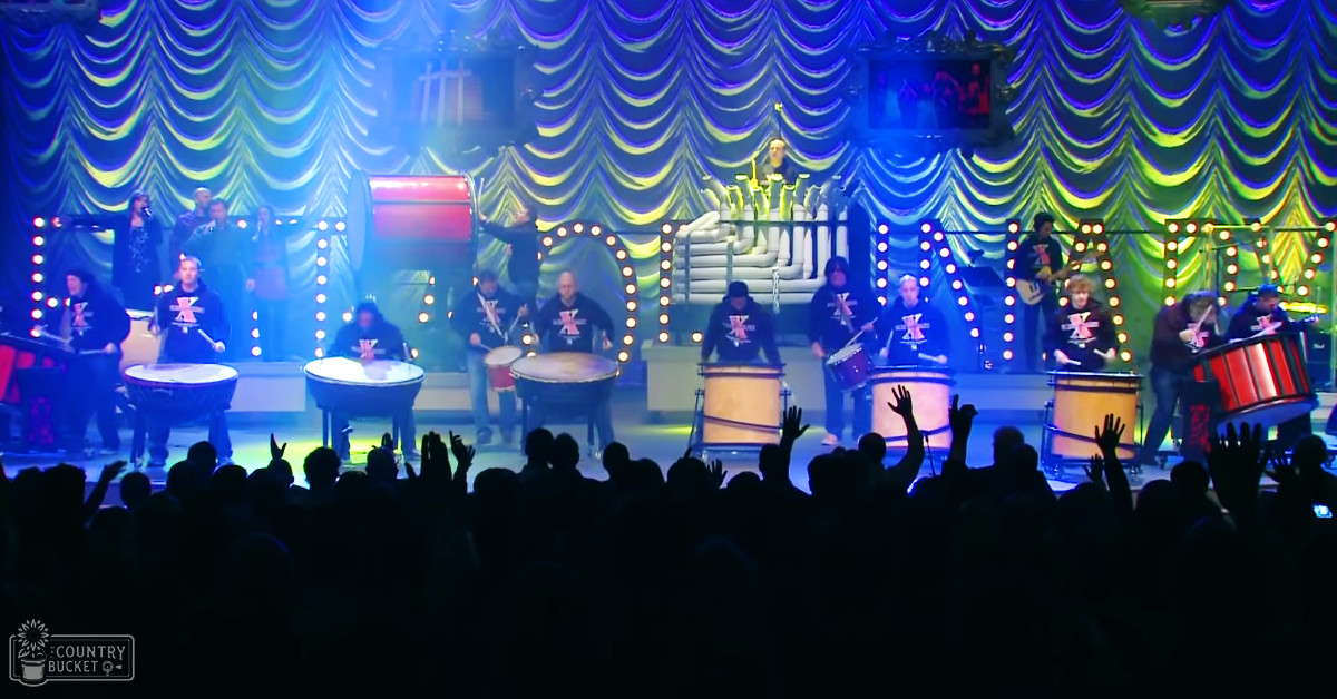 A lively concert performance in a theater with multiple musicians engaged in playing percussion instruments under vibrant stage lighting.