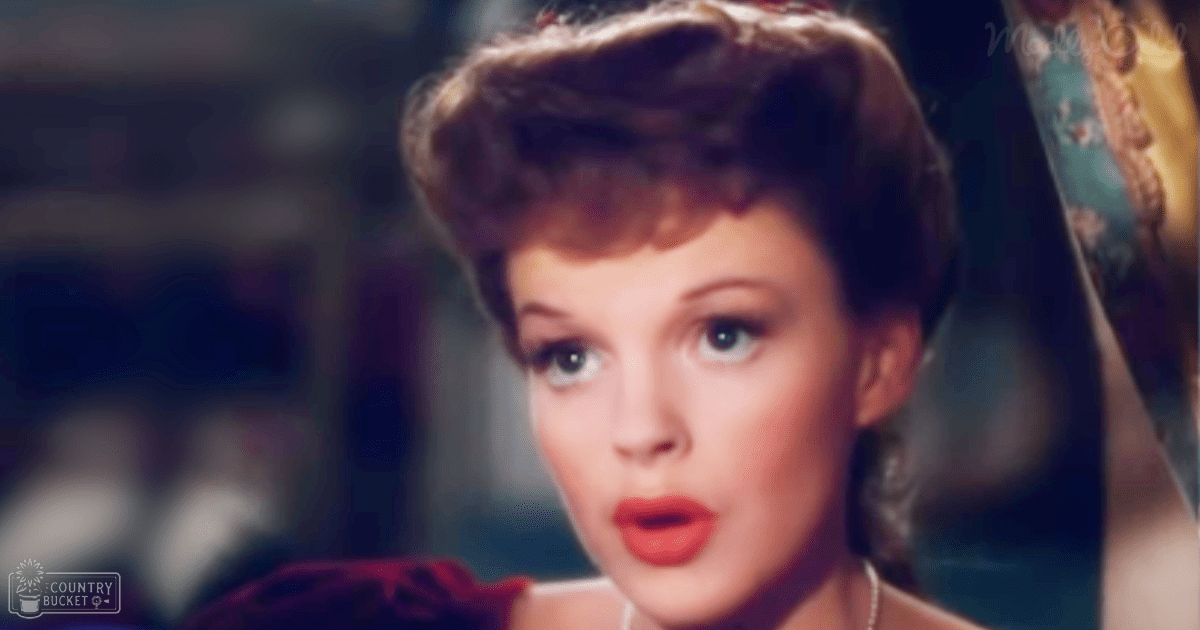 A young adult female wearing a red mid-20th-century style garment with short sleeves and high neckline, accessorized with a necklace, indoors at what appears to be an event or gathering.