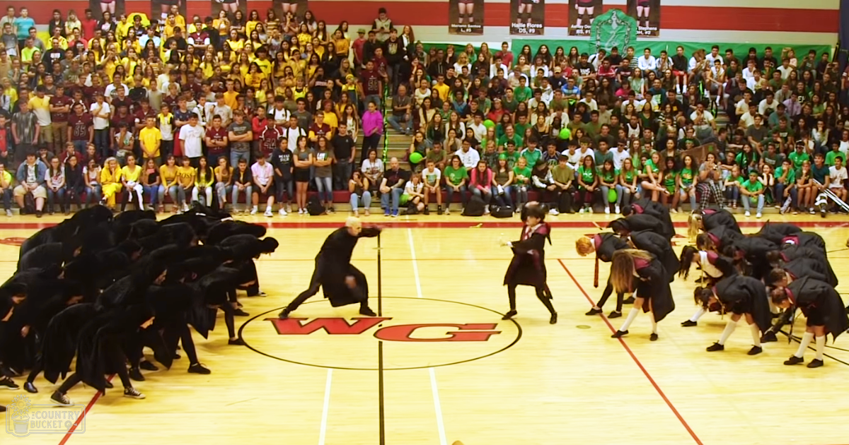 A dance performance by young adult female dancers in a school gymnasium with an audience seated on bleachers.