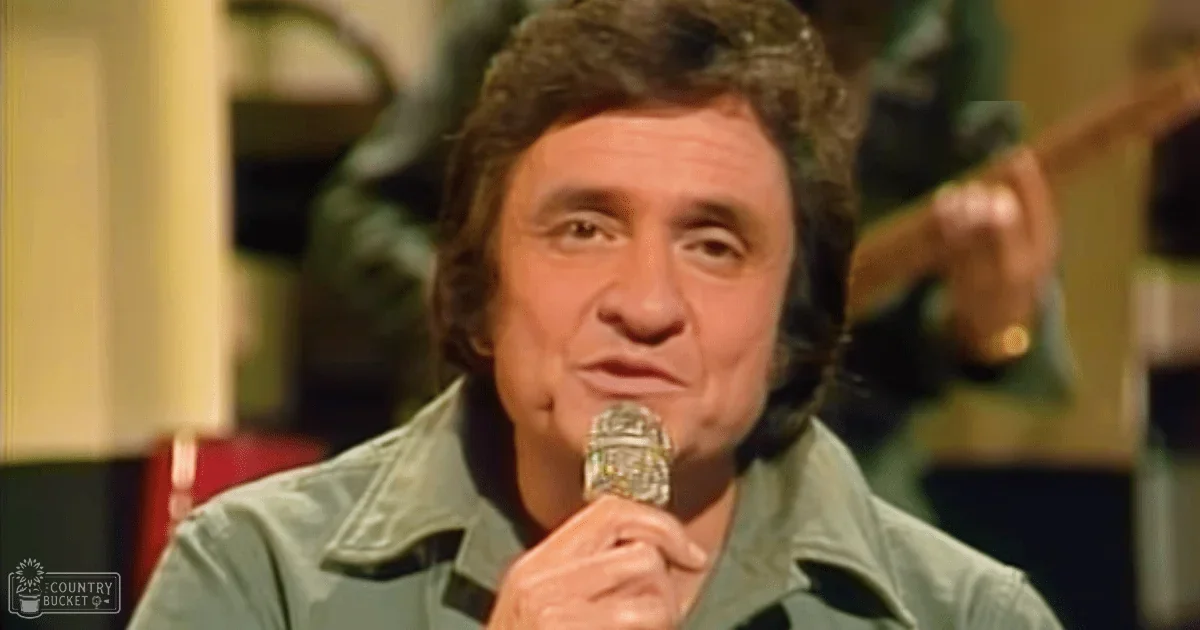 A middle-aged man in a light green denim-like jacket indoors, with warm lighting and background elements suggesting a stage or studio setting.