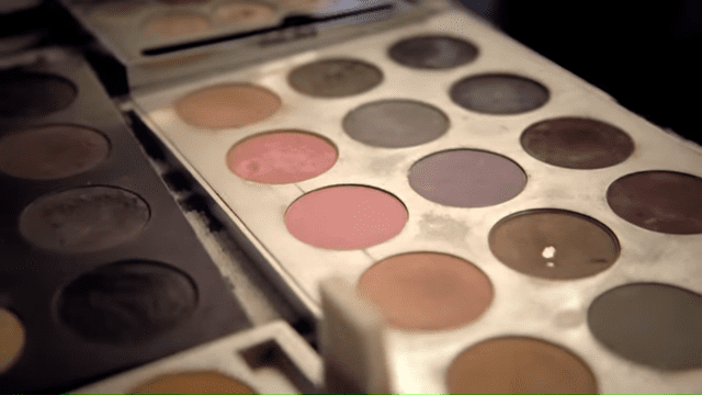 An open makeup palette with various shades of eyeshadow and blush, indoors setting with a dark backdrop.