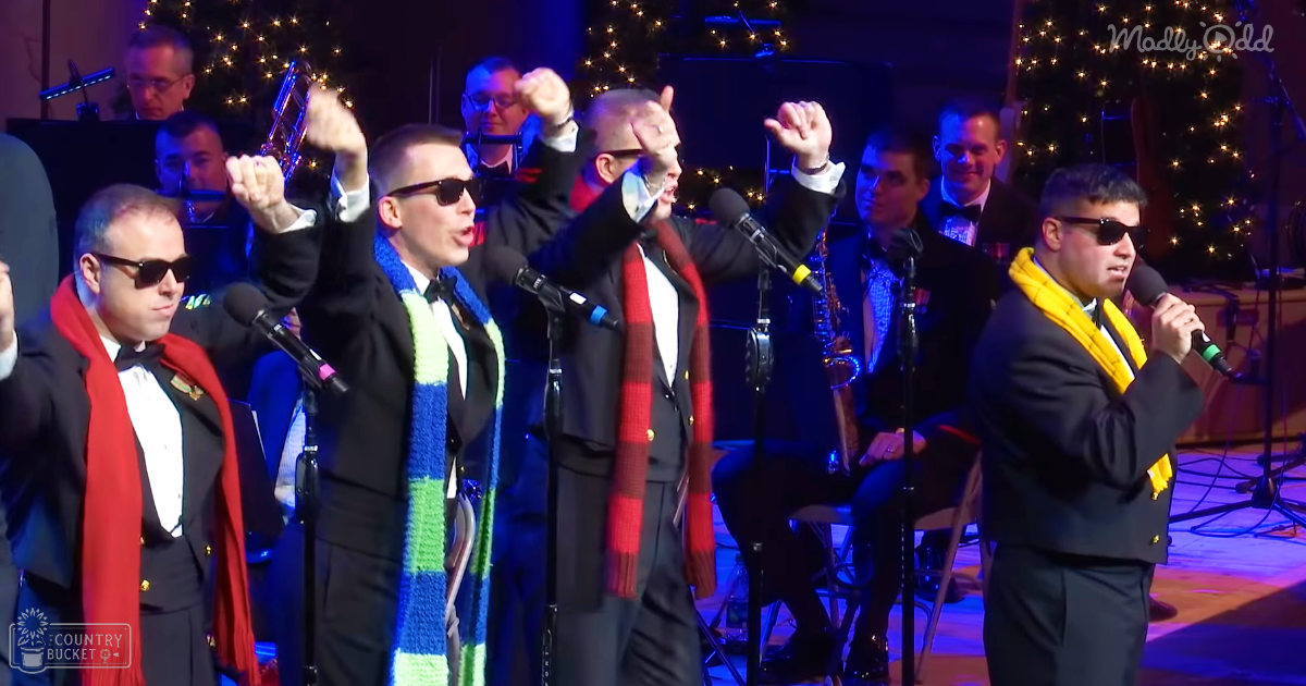 A group performance in an indoor setting during a holiday event with performers wearing black suits and colorful scarves, surrounded by Christmas lights.