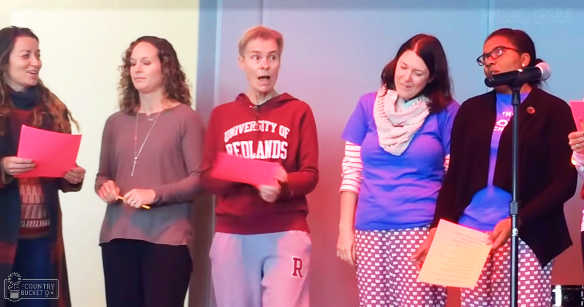 A group of adult females and males performing indoors, wearing various casual outfits with accessories like scarves and jewelry.
