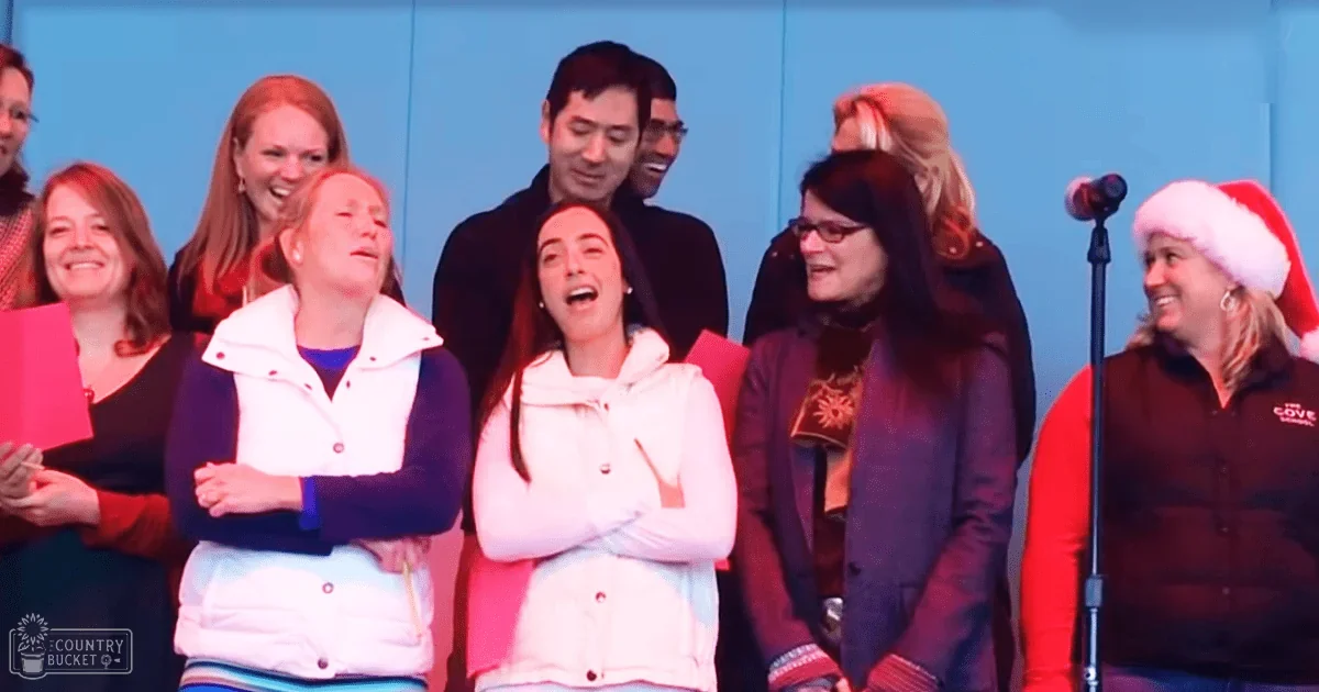 Adults participating in a singing event indoors with a simple blue backdrop; even lighting suggests evening or night.