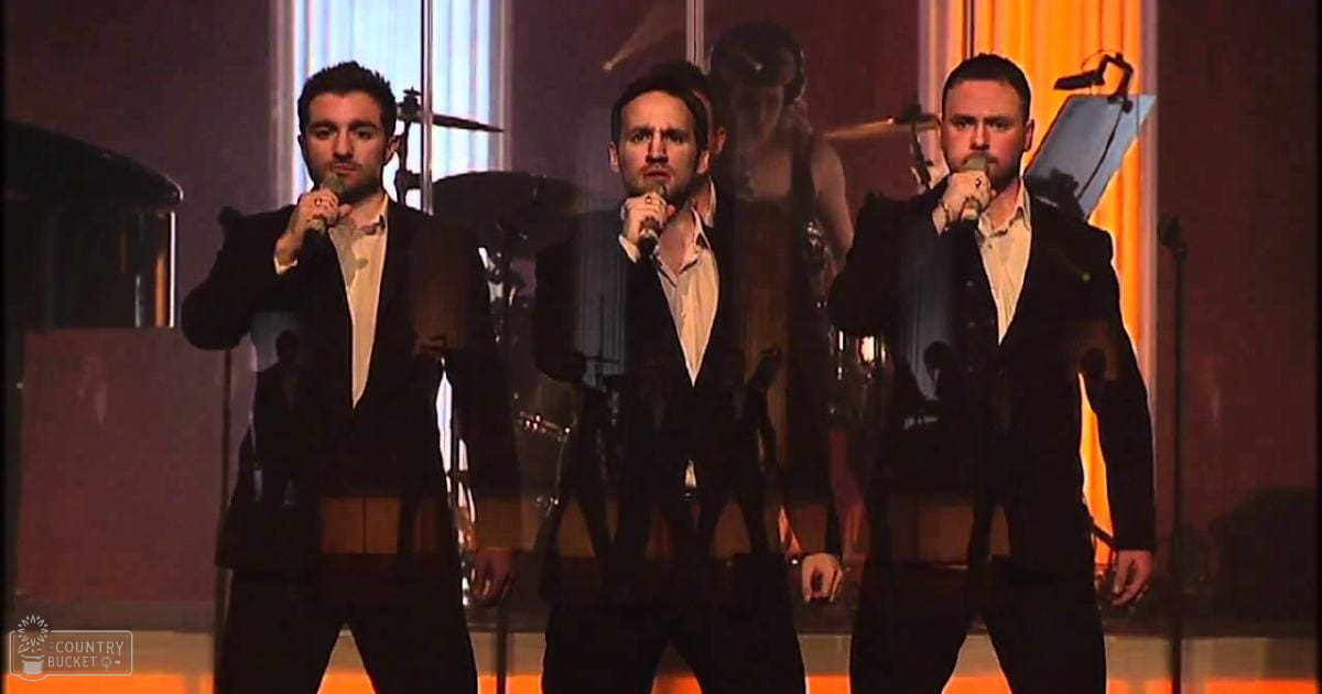 Musical performance group on a stage with microphones, drums, and cymbals visible behind them under formal indoor lighting.