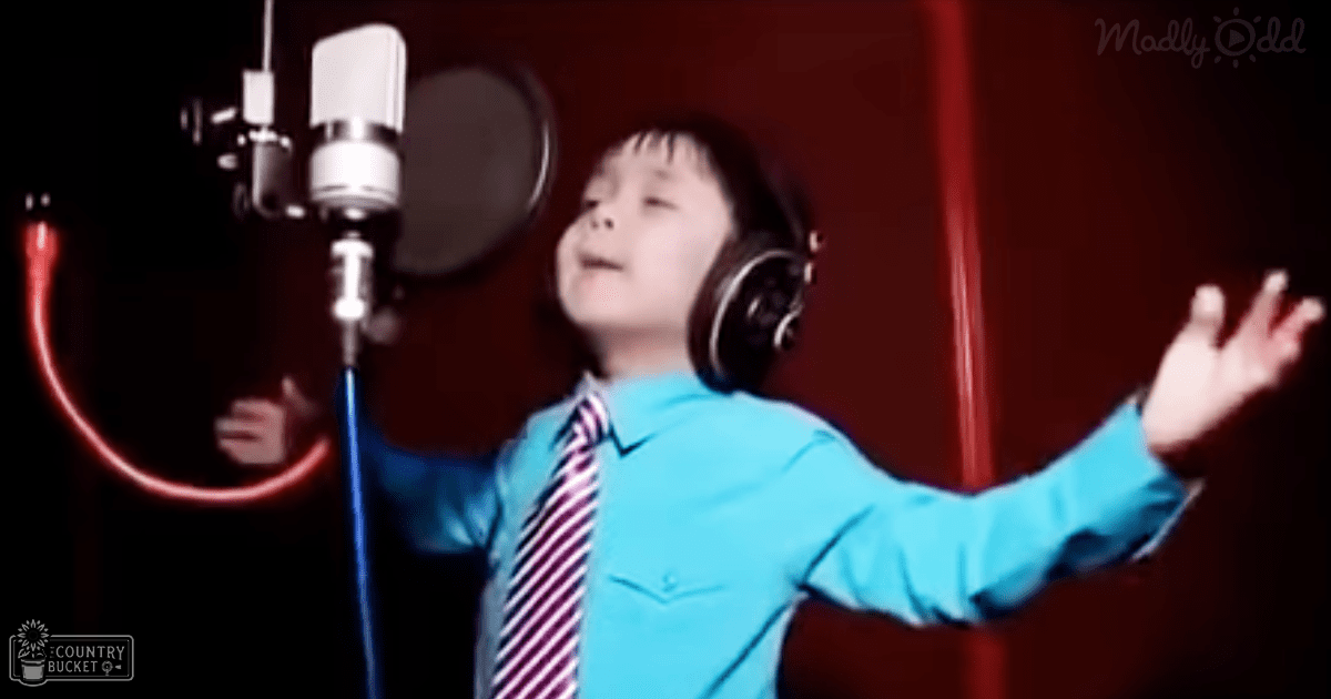 A 5-8 year old male child in a recording studio, wearing a light blue button-up shirt with long sleeves and a pointed collar.