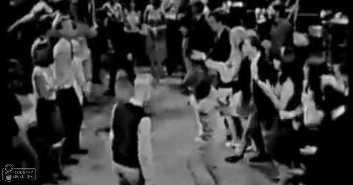 Children of various ages dressed in school uniforms or casual attire dance on a dance floor at night with artificial lighting.