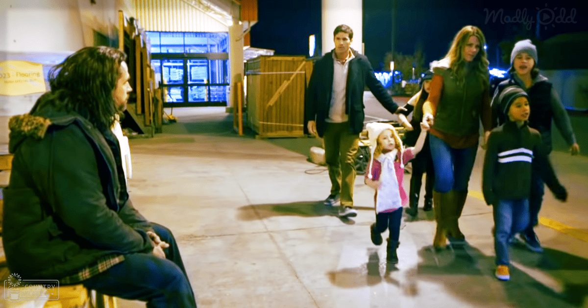 A family walks together in an outdoor nighttime scene with illuminated windows and paved ground.