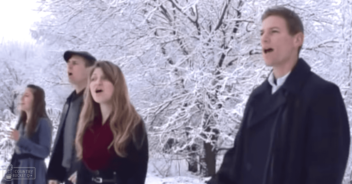 Young adult male and female singing in a snowy outdoor setting with white snow-covered trees under natural daylight.