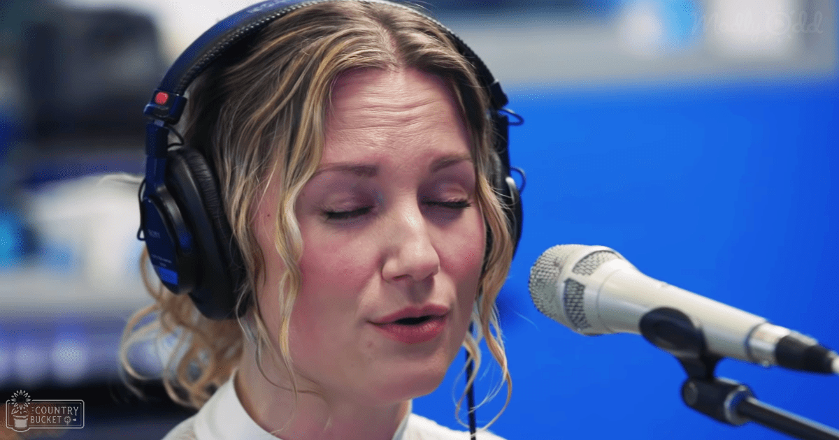 Young adult female in a radio studio, wearing a collared white shirt with short sleeves and black headphones with red accents.