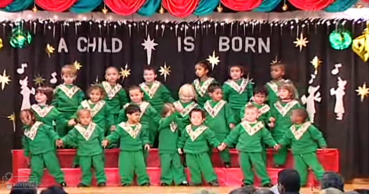 Children performing in a festive school setting with bright green pajamas or costumes, red curtains, and a stage backdrop reading 'A CHILD IS BORN'.