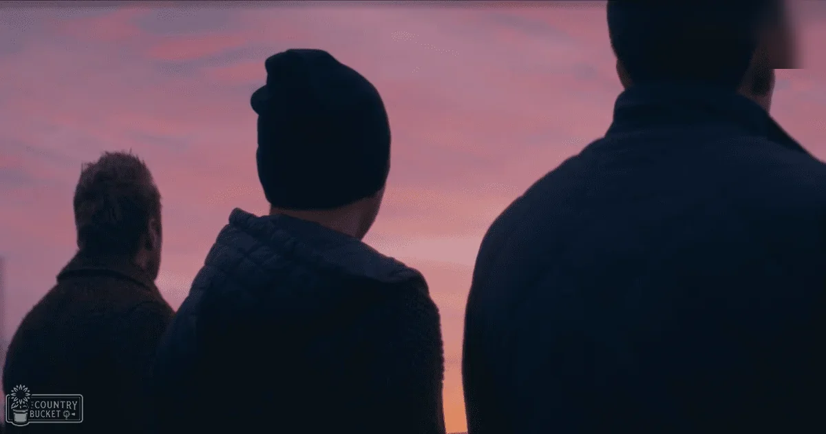 Three adult males standing outdoors during twilight in a park-like setting with a gradient sky transitioning from pink to dark shades.