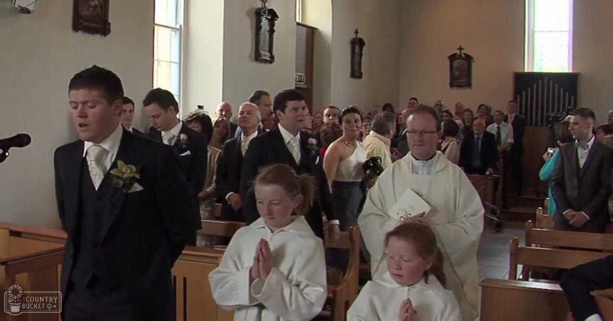 A wedding ceremony inside a church with wooden pews, religious decorations, and natural light streaming through large windows. Guests are dressed formally for the occasion.