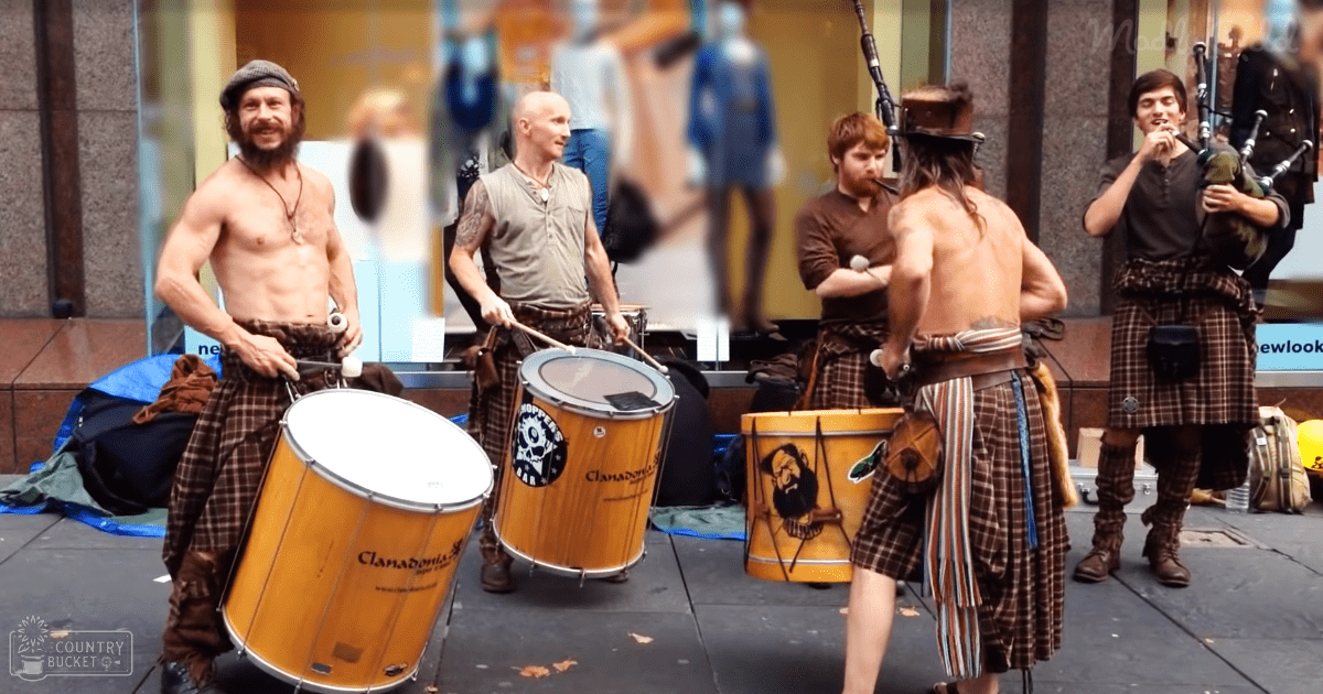 Street performance with drummers in plaid kilts and mannequins displayed behind them.